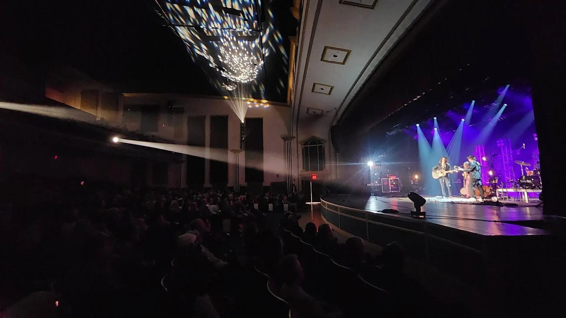 A concert at the Celestia Theater seen from the back of the house, stage lit in purple and blue