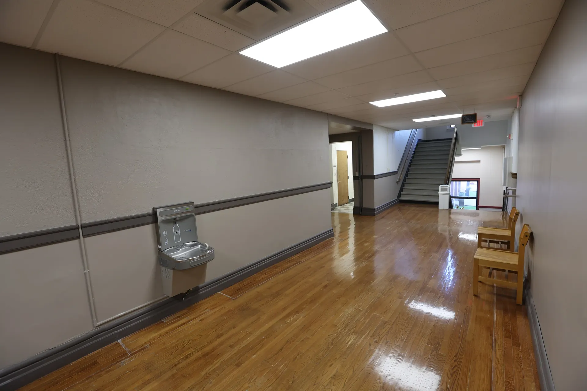 A corridor with the original drinking fountain and wood benches, the stairs beyond