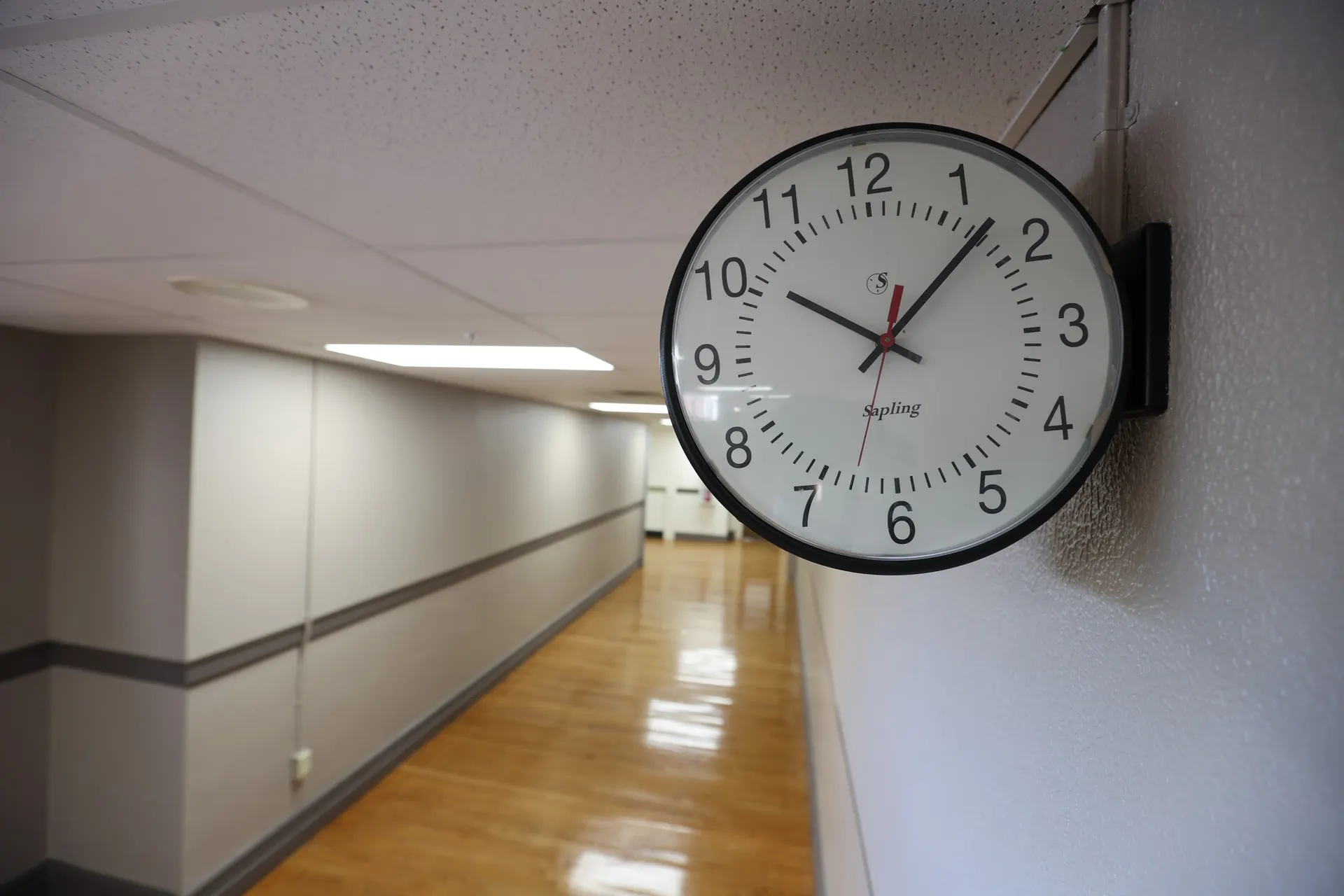 The original school clock on a corridor wall, the hallway stretching behind it