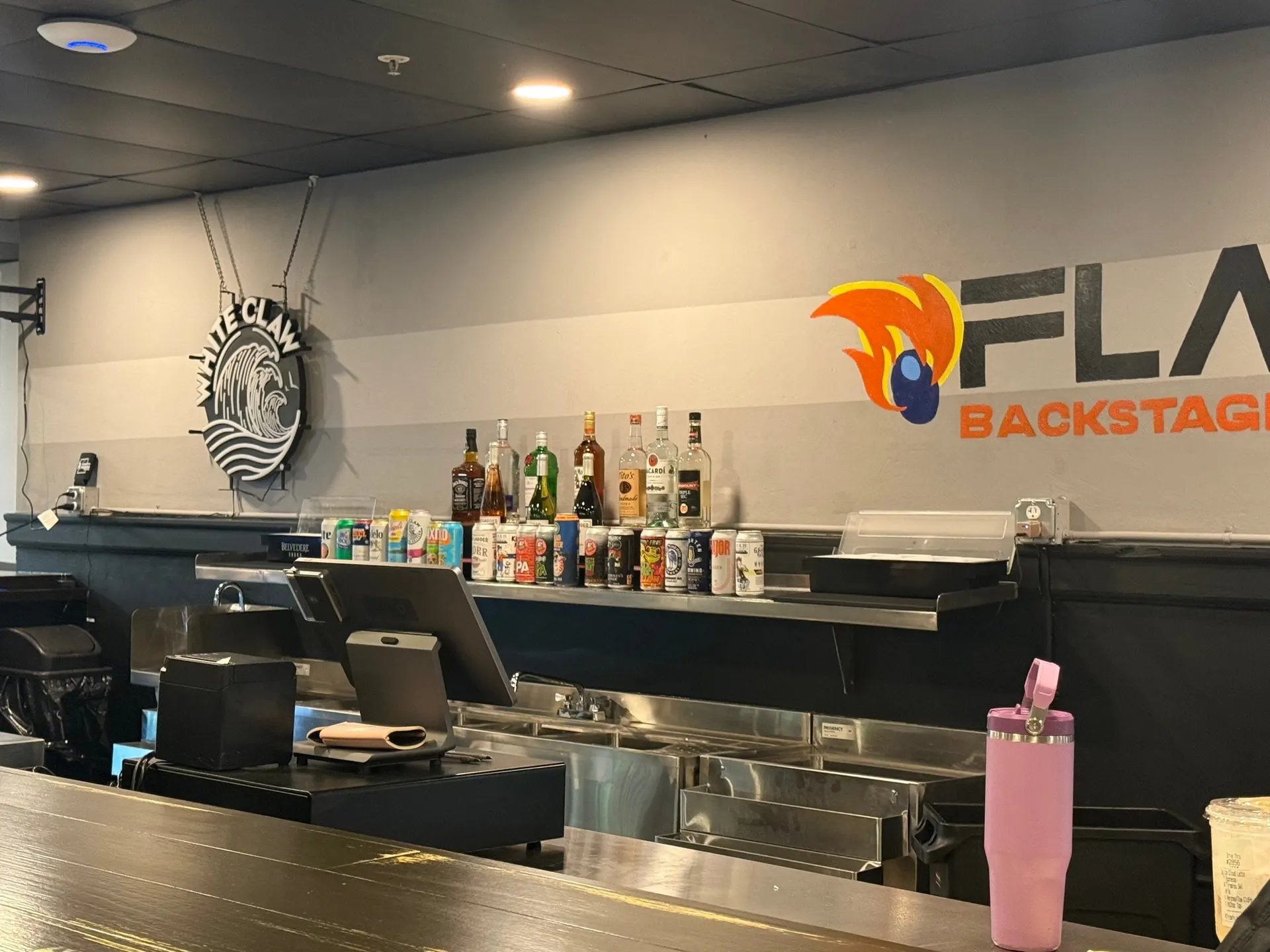 The bar at Flame Backstage Grille & Bar, bottles on the back shelf and the Flame logo behind