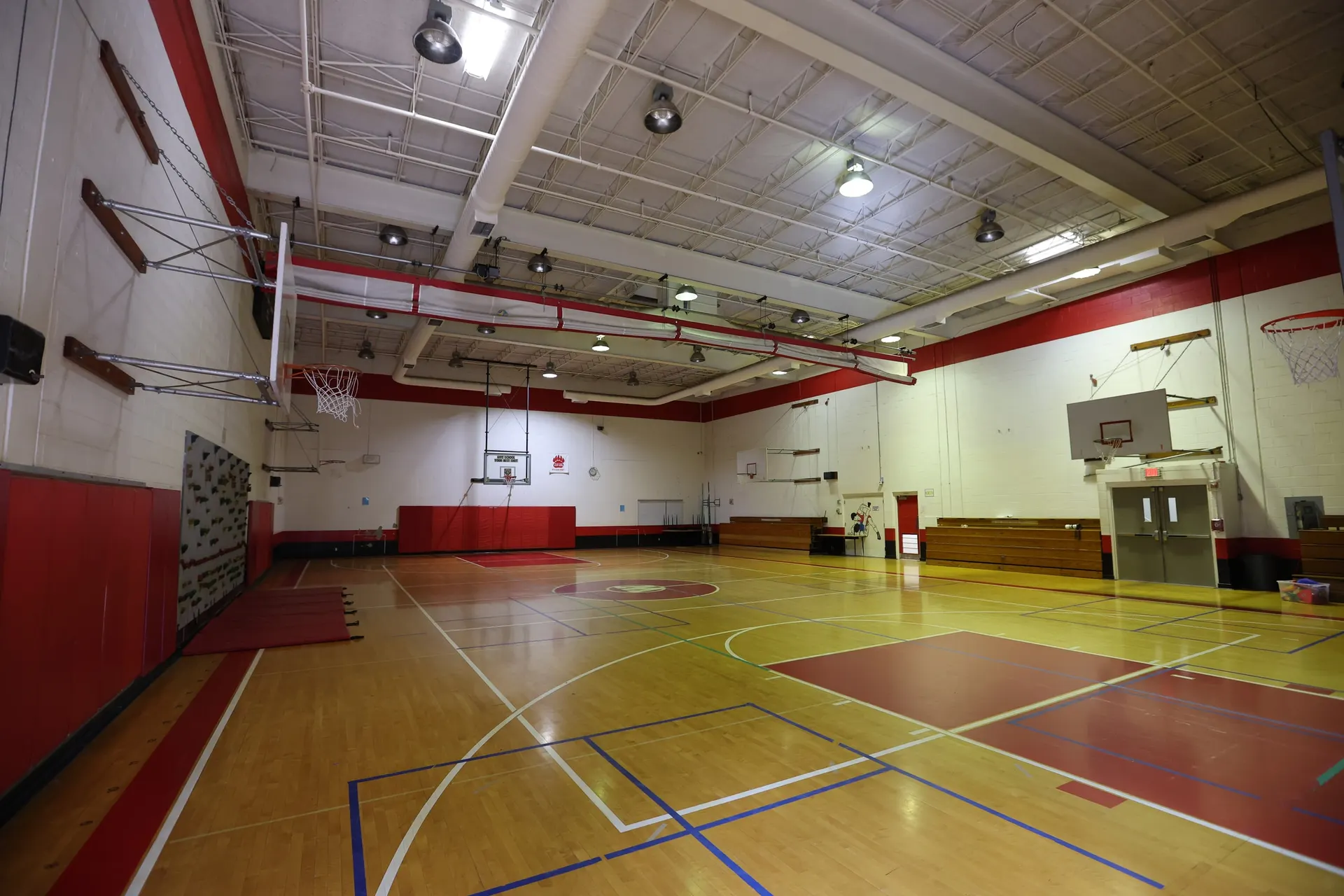 The lower-level gym from the sideline, hardwood court, red trim and basketball hoops