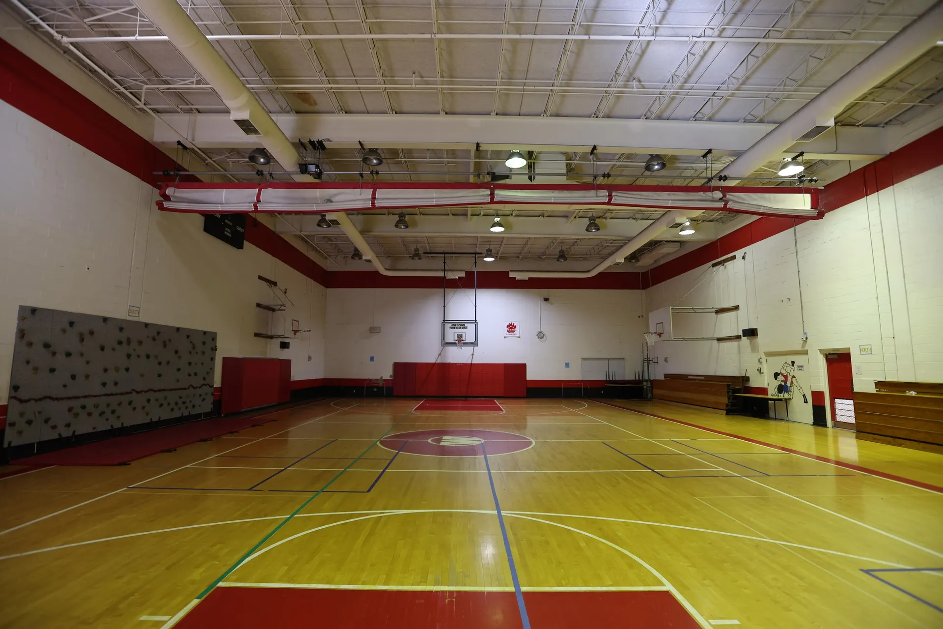 The lower-level gym, a full hardwood court with red trim and basketball hoops