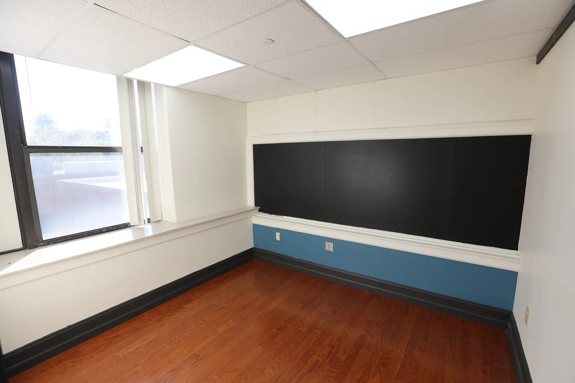 A corner office with blue wainscot, a chalkboard and a window over the square