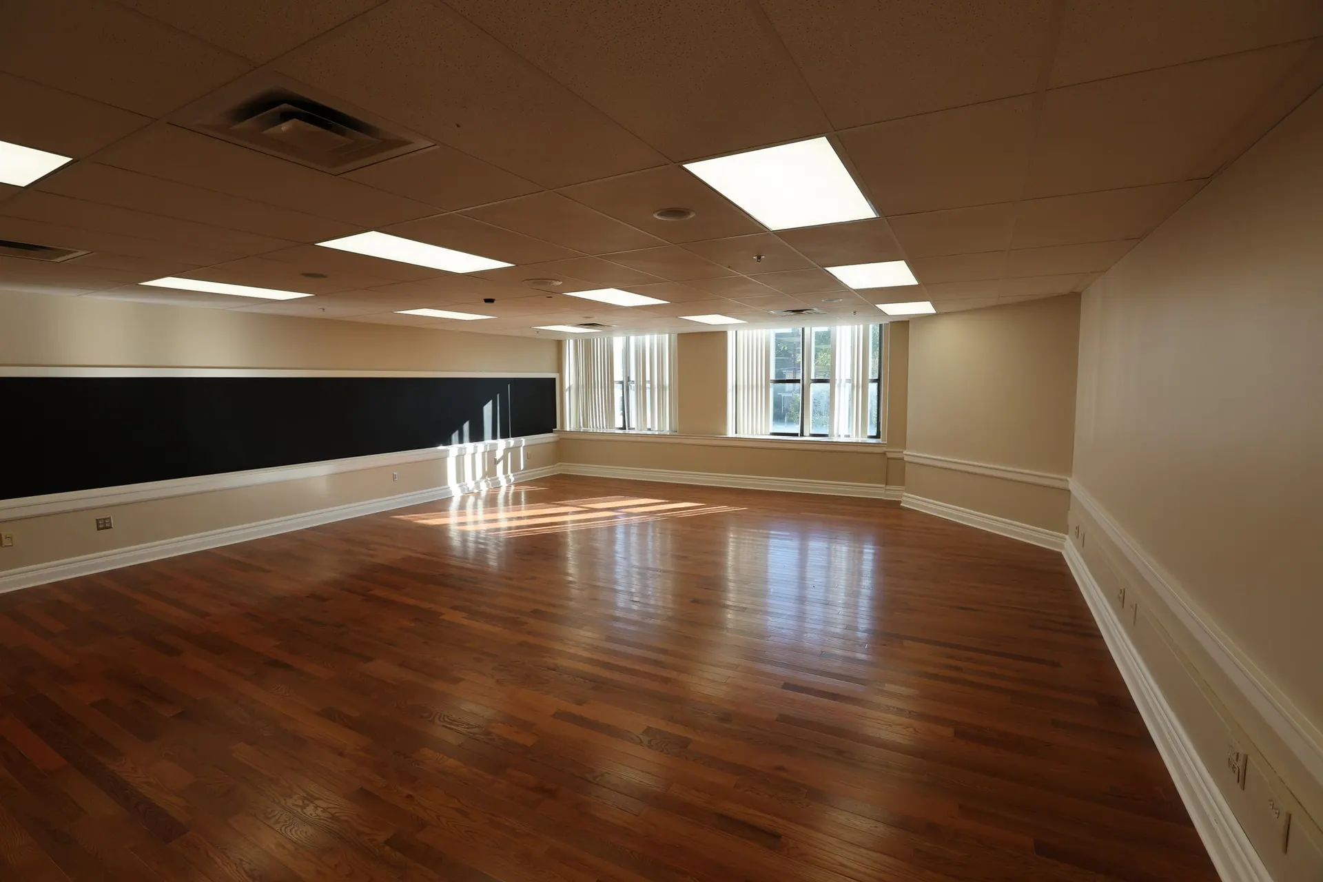 A wide suite with its original chalkboard, sun on the hardwood floor and windows down one side