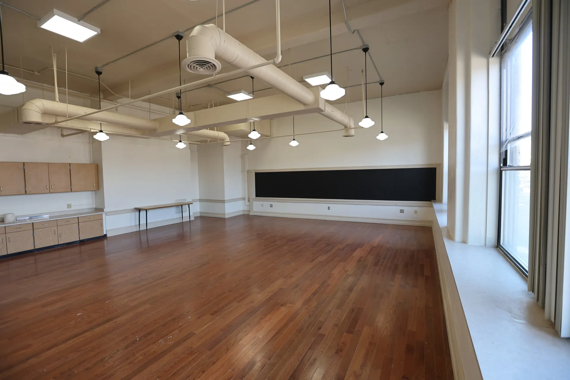 An open suite with hardwood floors, built-in cabinets and pendant lighting under exposed ductwork