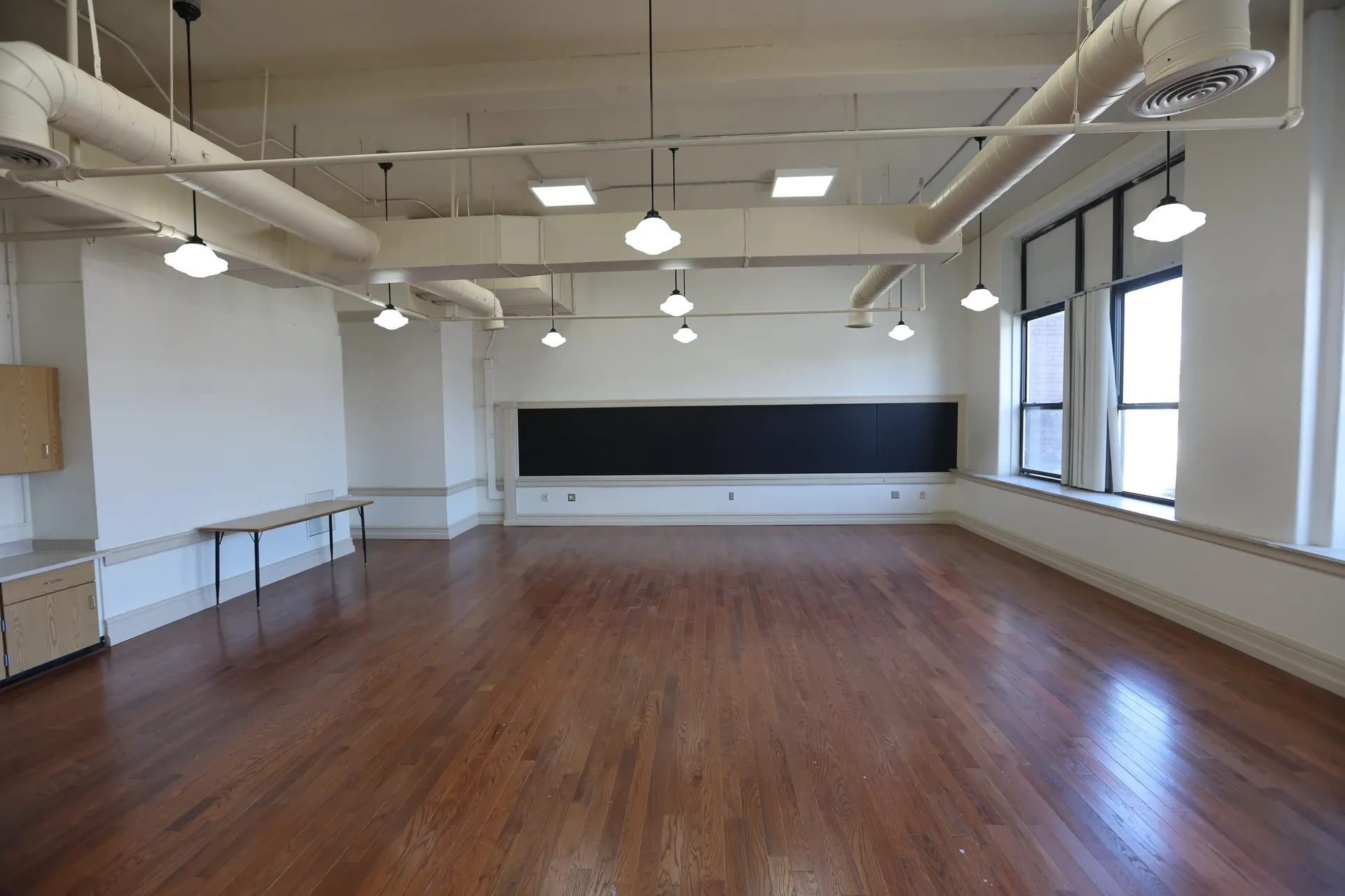 An open suite with pendant lights, a chalkboard and a wall of tall windows over hardwood floors